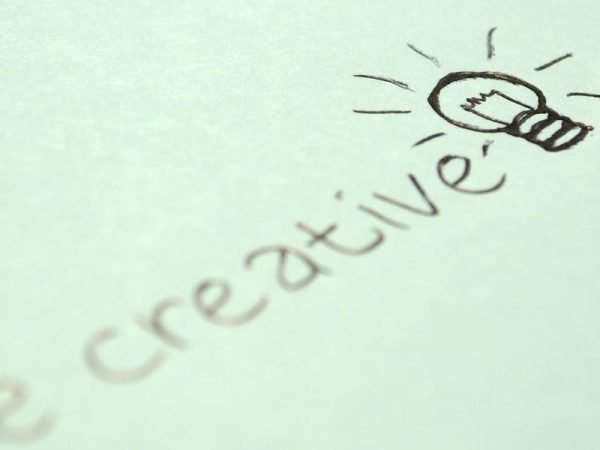 Close-up of handwritten 'Be creative' with a light bulb sketch on paper.